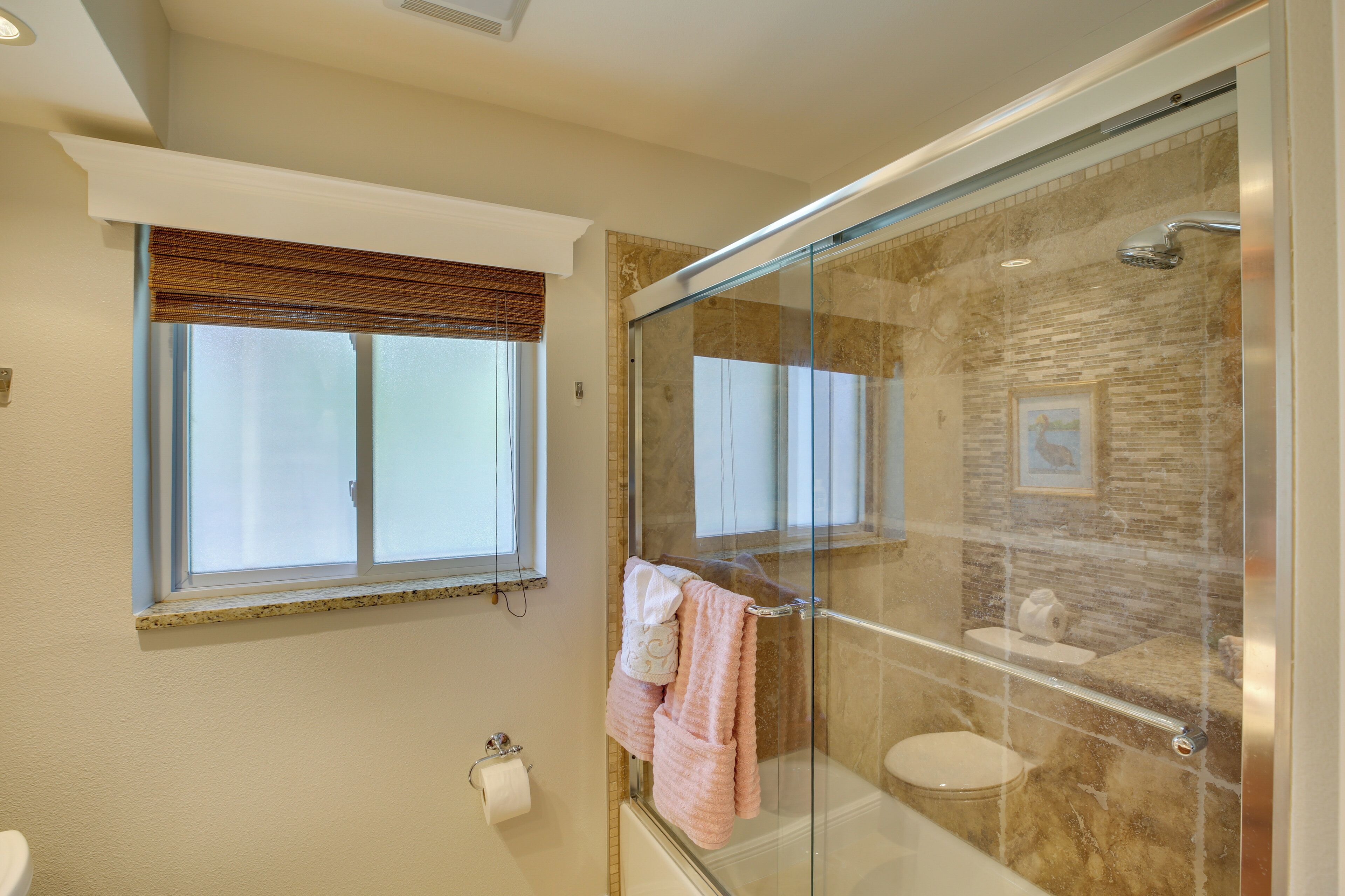 A modern bathroom with a glass-enclosed shower, a toilet, and a window with blinds.