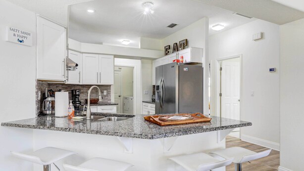 A modern kitchen with white cabinets, a granite countertop, and a stainless steel refrigerator.