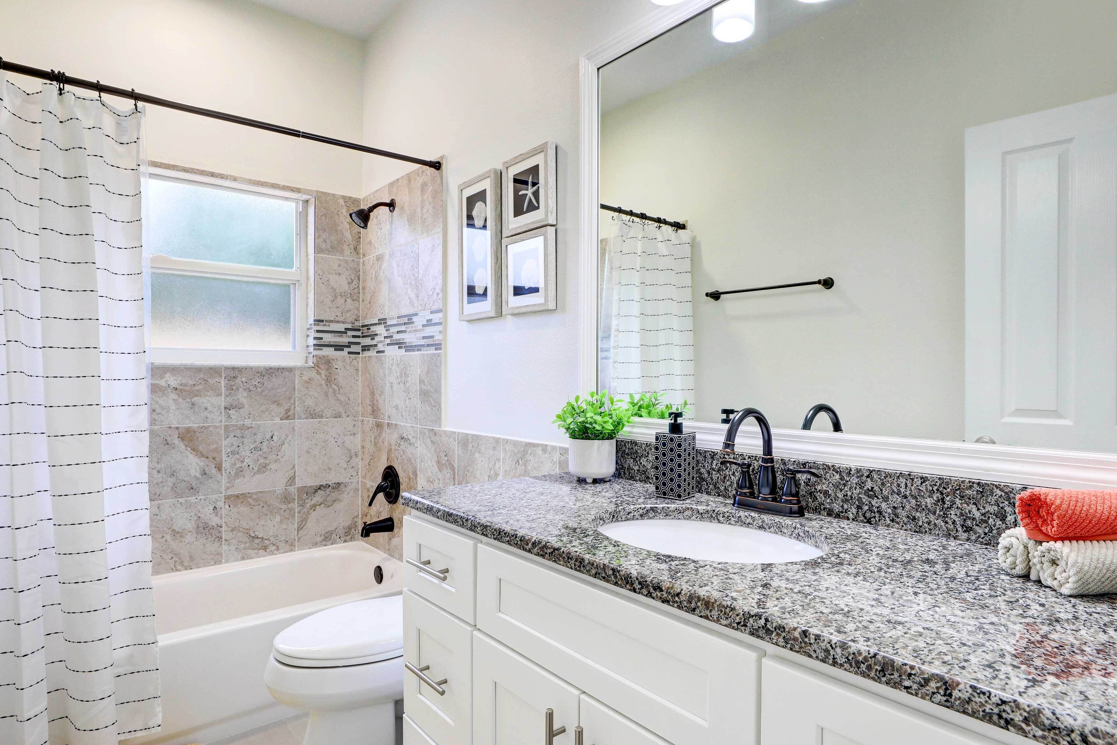A bathroom with a white toilet, a sink with a granite countertop, a large mirror, and a shower curtain.