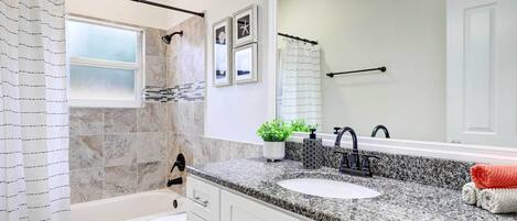 A bathroom with a white toilet, a sink with a granite countertop, a large mirror, and a shower curtain.