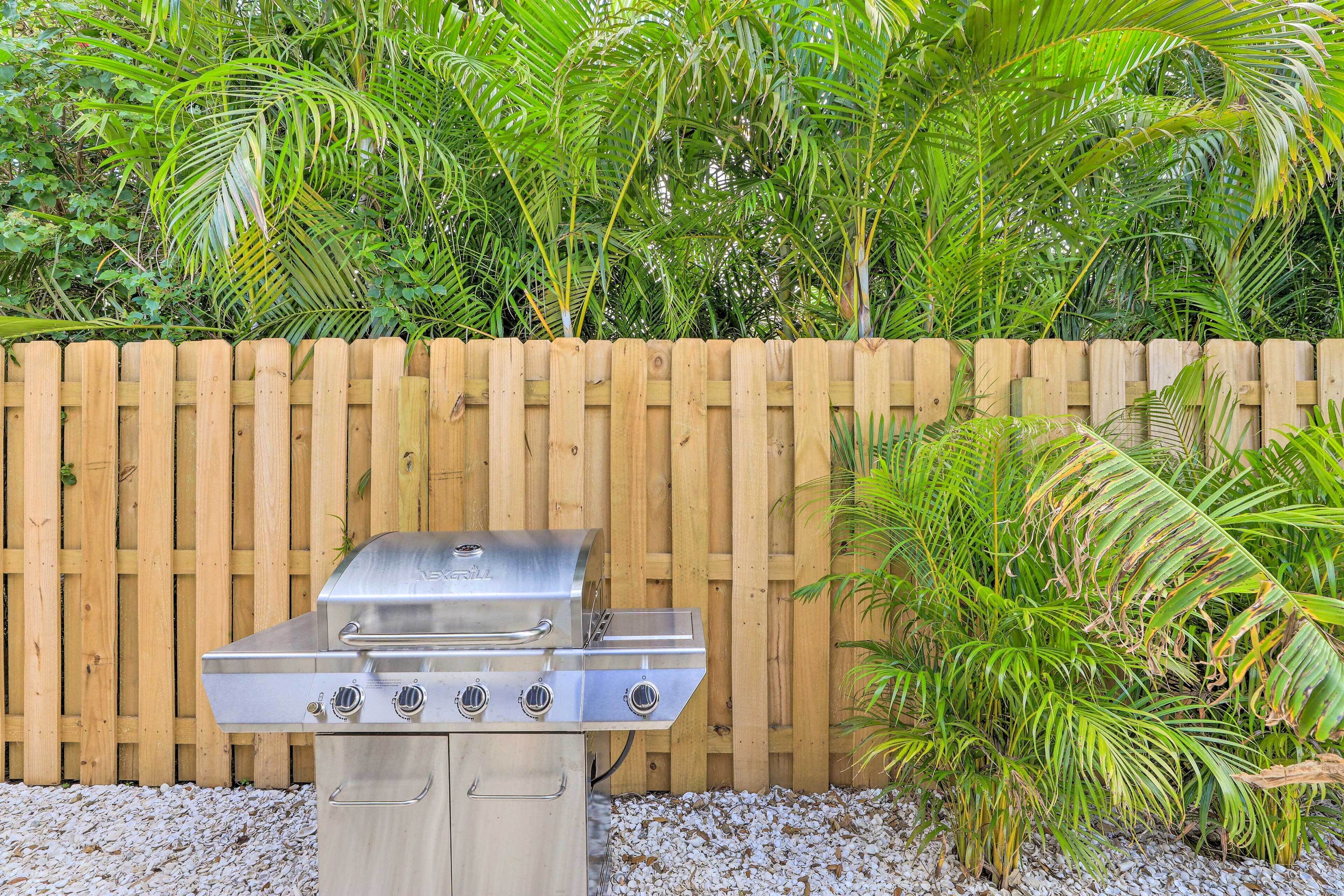 A stainless steel barbecue grill with four burners, positioned on a gravel surface.