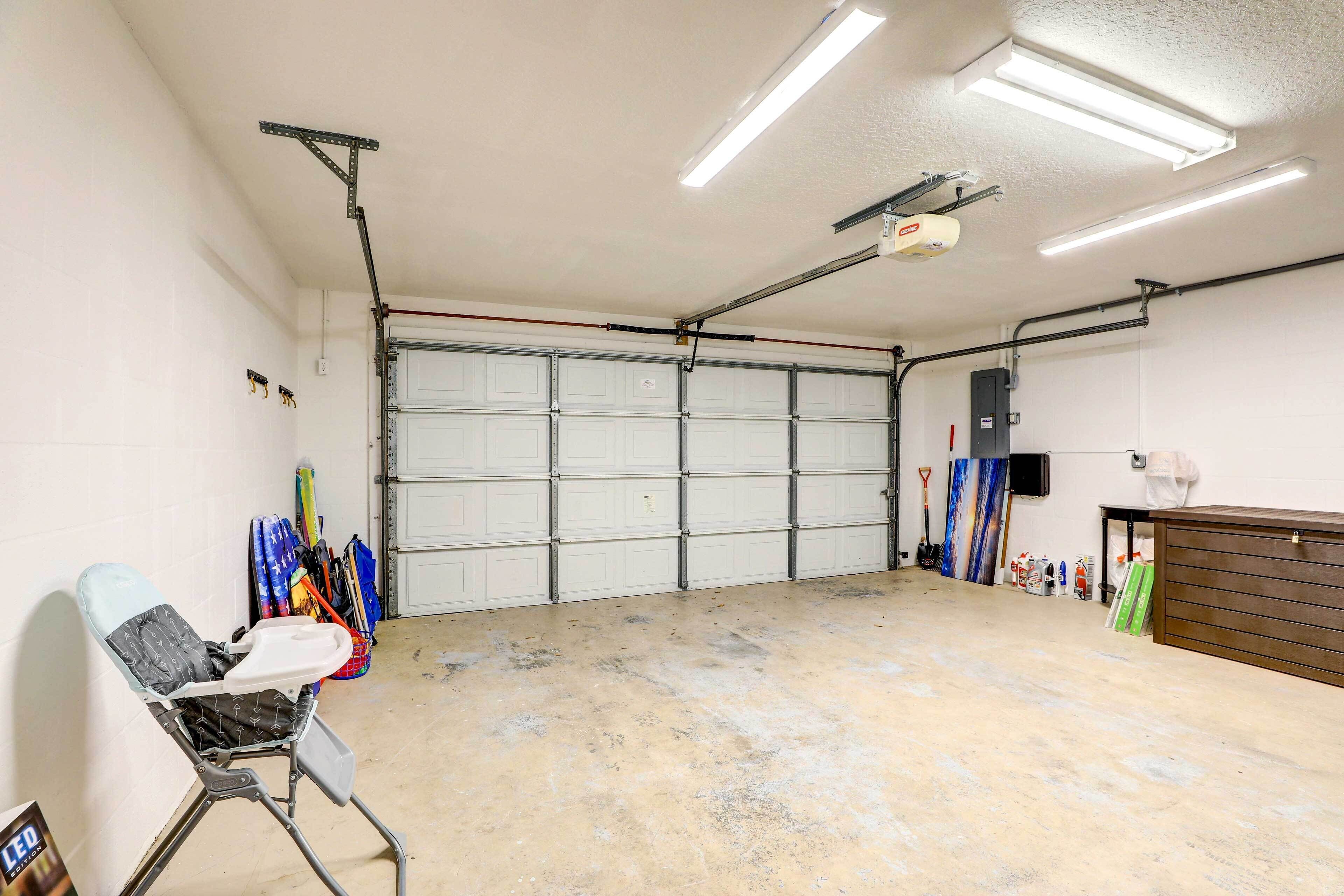 A garage with a concrete floor, a white garage door, and various tools and equipment stored against the wall.