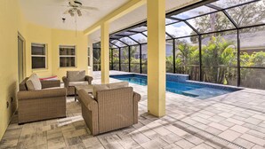 A covered patio area with wicker furniture, a pool, and a view of greenery.