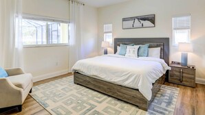 A bedroom with a large bed, a nightstand, a chair, and a window with blinds.