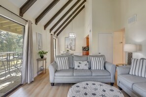Uma sala de estar moderna com um conjunto de sofá cinza, uma mesa de centro redonda com padrão náutico e uma área de jantar visível através de uma porta de vidro.