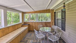 A sunroom with a glass table and white chairs, a bench, and large windows with a view of greenery. - Bright Steinhatchee Home: Proximity to Ocean! (Steinhatchee)