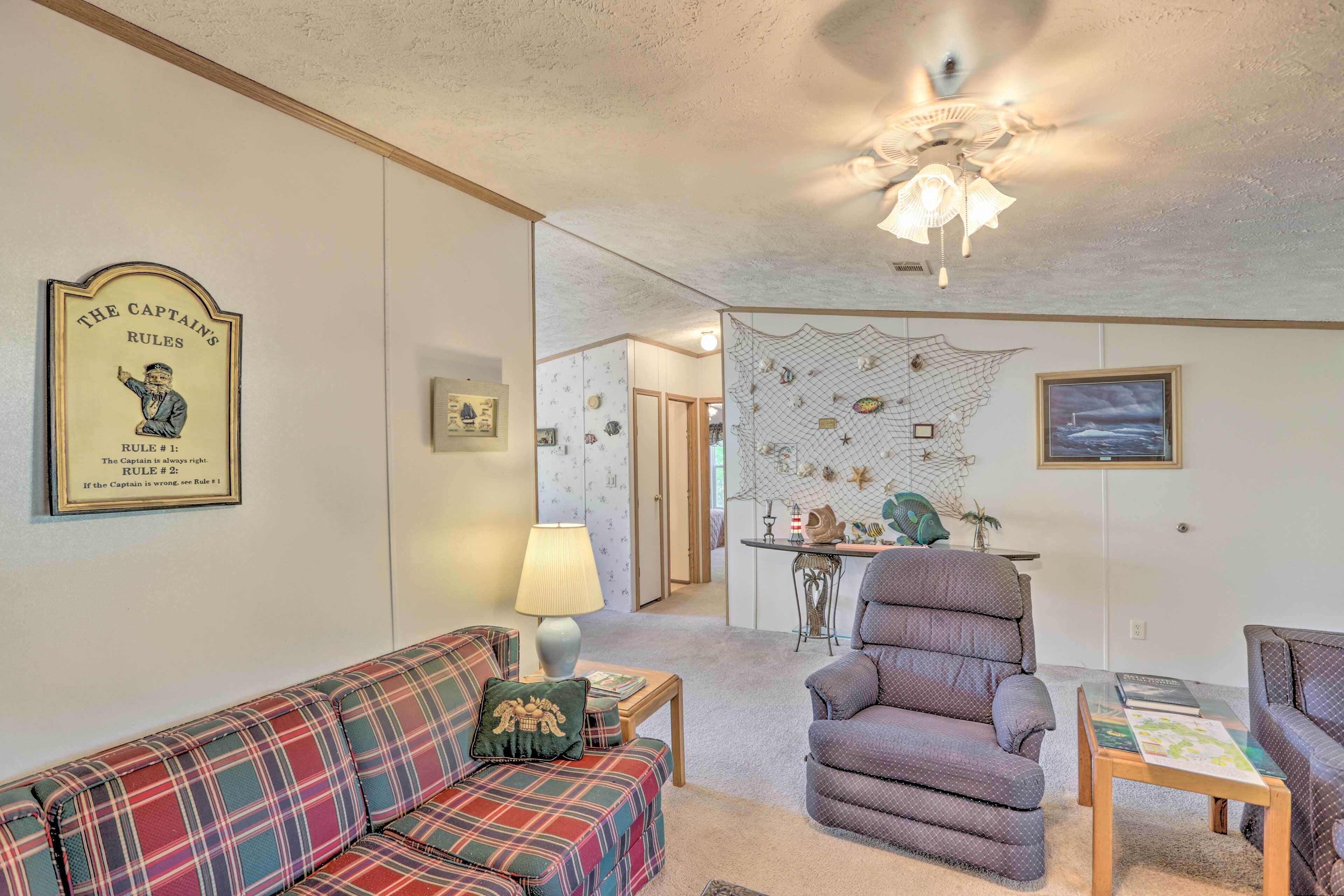 A living room with a plaid sofa, a patterned armchair, a table with a lamp, and a ceiling fan.