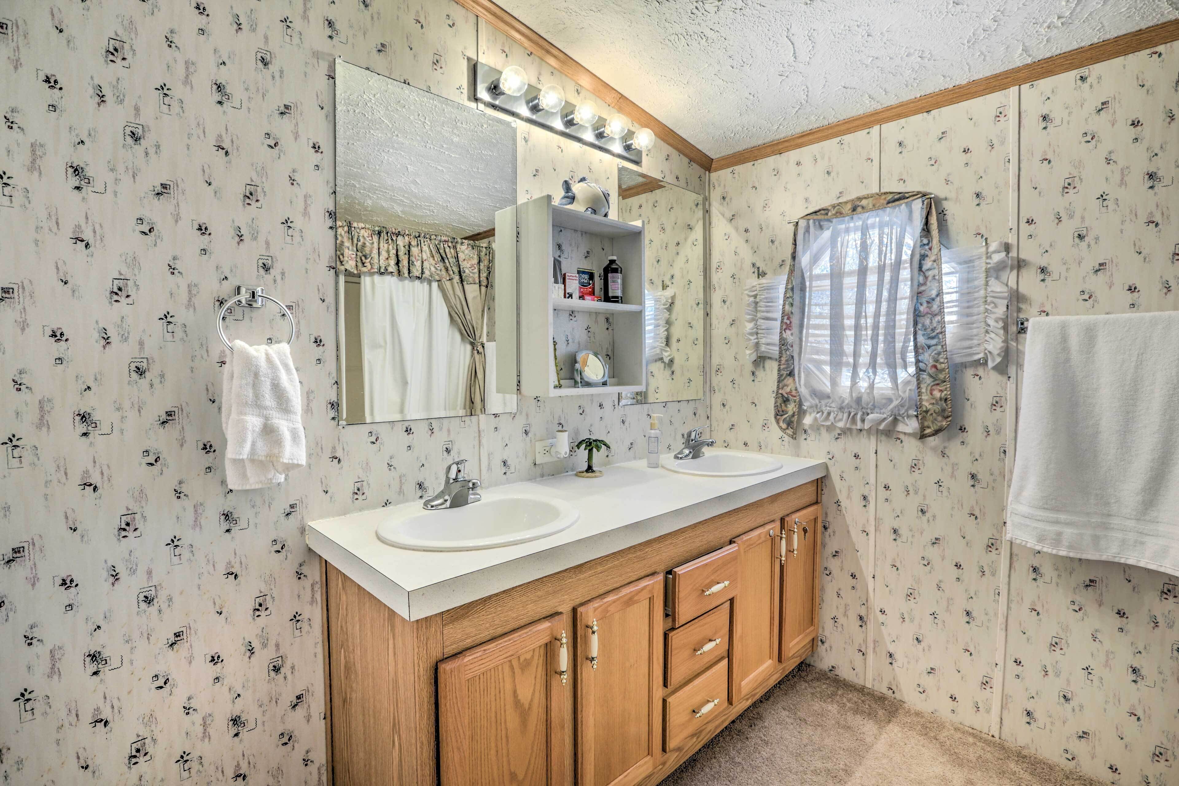 Ein Badezimmer mit zwei Waschbecken, Holzschränken, einem beleuchteten Spiegel und blumigem Wandpapier.