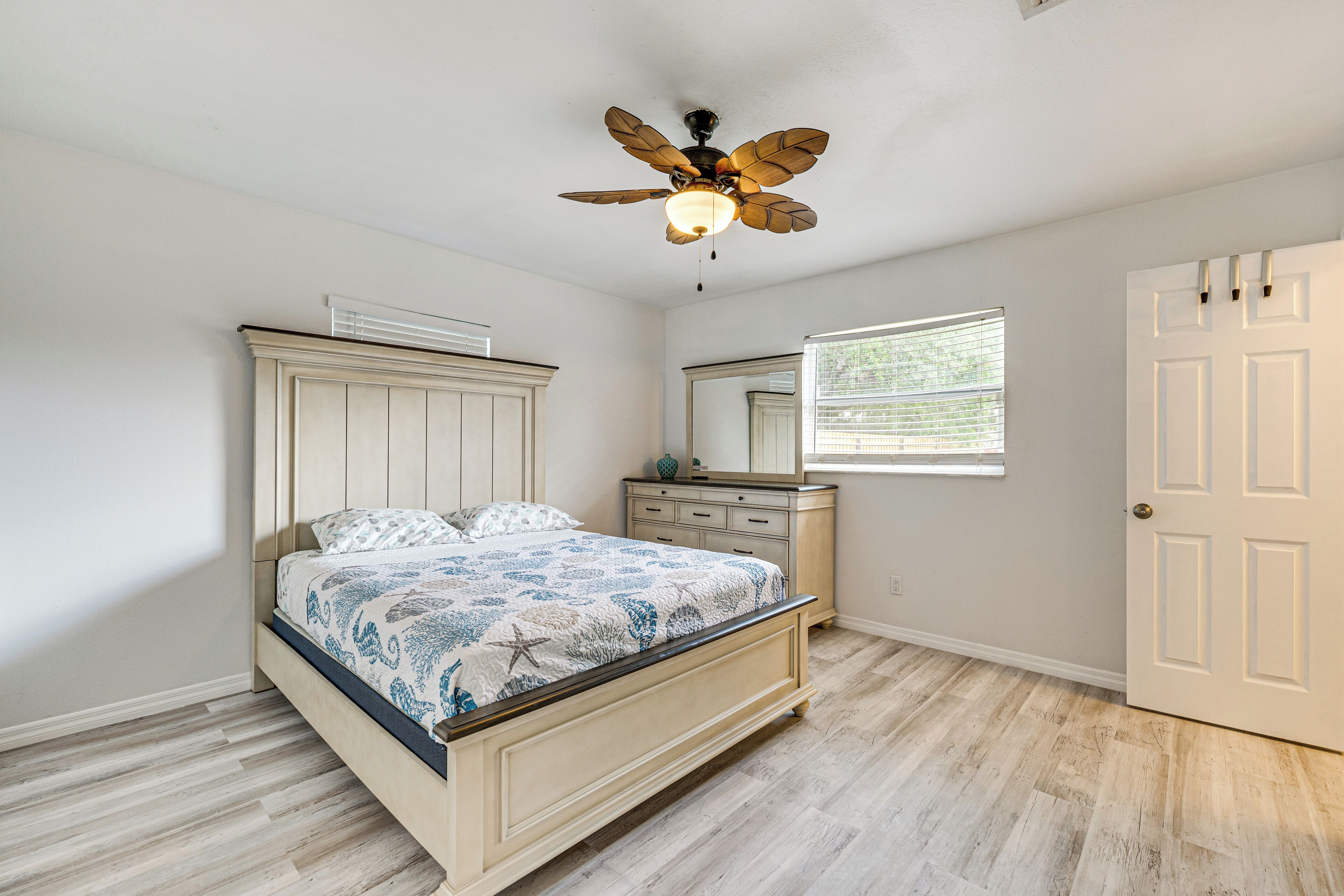 A bedroom with a bed, dresser, mirror, ceiling fan, and a door.