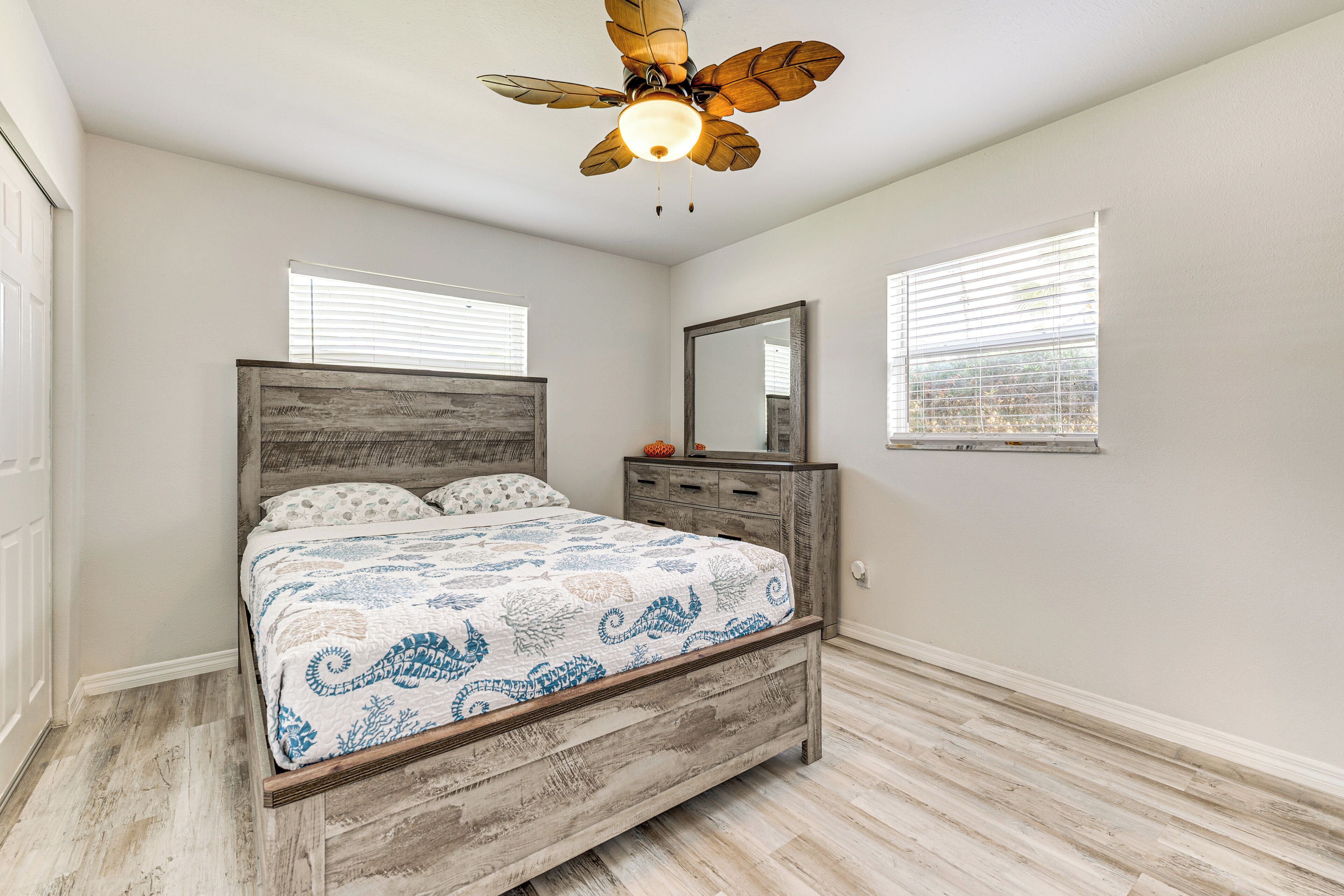 A bedroom with a wooden bed, a ceiling fan, and two windows with blinds.