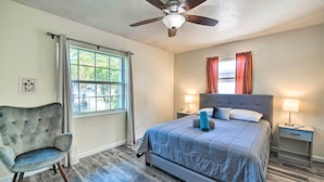 Une chambre à coucher comprenant un lit, une chaise, un ventilateur de plafond, une fenêtre et une table de chevet avec une lampe.
