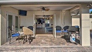 Un patio couvert avec un ventilateur de plafond, un barbecue et des sièges.