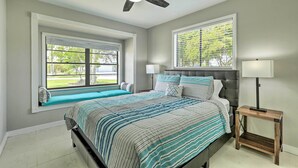 A bedroom with a bed, two windows, a ceiling fan, and a nightstand.