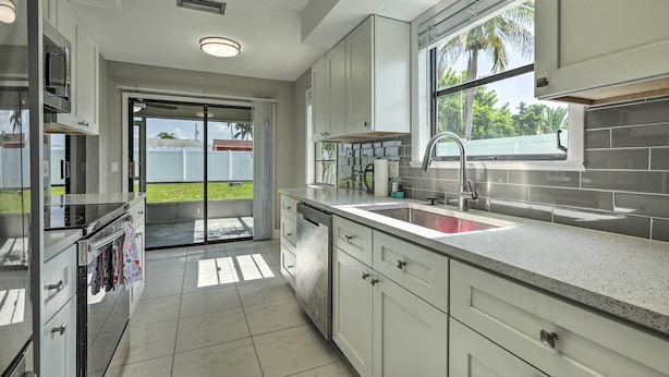 A modern kitchen with white cabinets, a stainless steel refrigerator, and a large window providing a view of the outdoors.