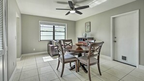 A dining area with a round table, four chairs, a ceiling fan, and a window with blinds.