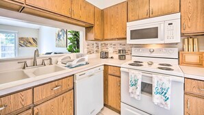 A modern kitchen with wooden cabinets, a white microwave, a dishwasher, and a stove. - Private Pool & Yard: Airy Kissimmee Retreat! (Poinciana)