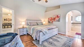 A bedroom with a bed, nightstands, a ceiling fan, and a view of the bathroom. - Private Pool & Yard: Airy Kissimmee Retreat! (Poinciana)
