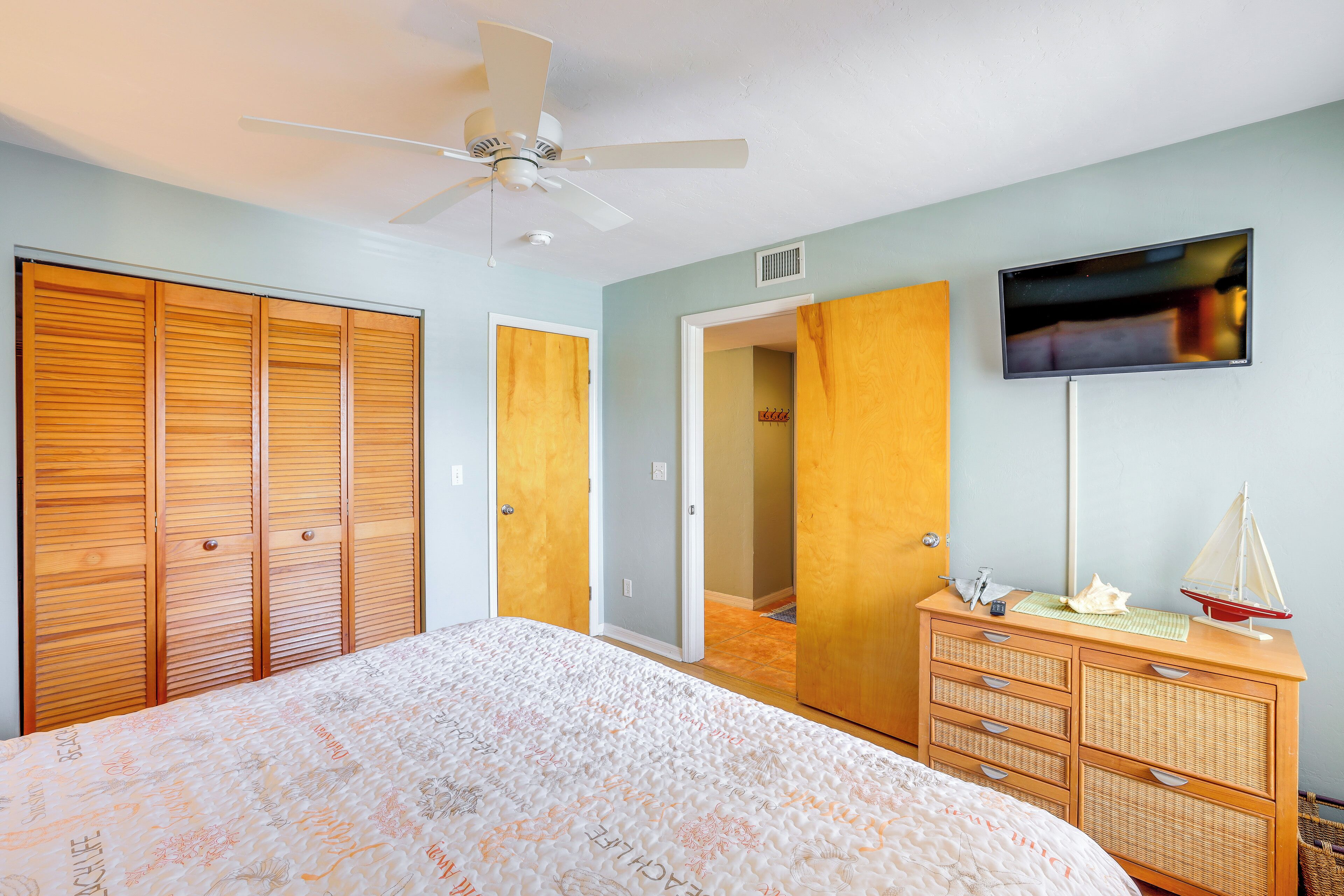 A bedroom with a bed, wooden wardrobe, dresser, television, and a ceiling fan.