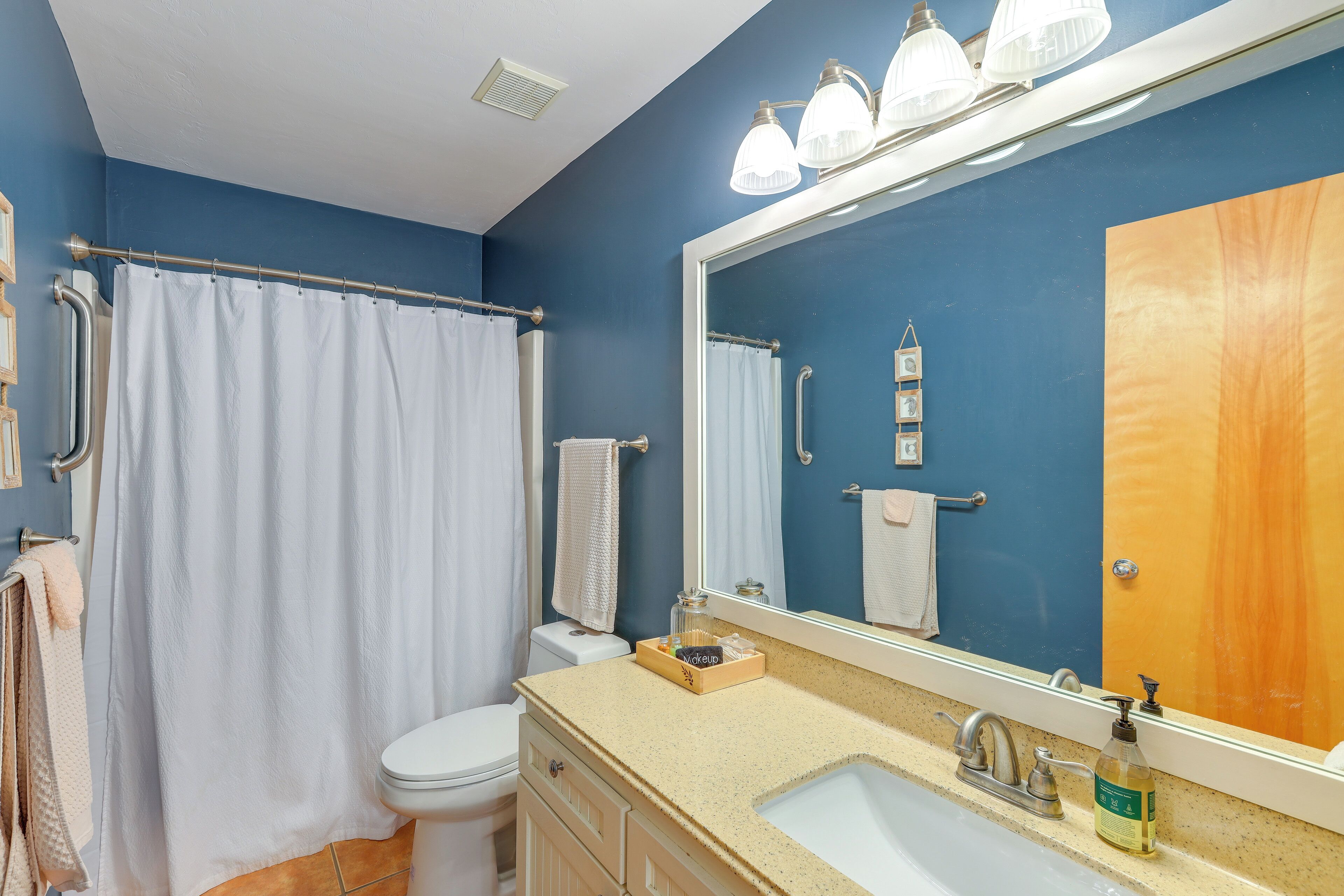 A bathroom with a shower curtain, a toilet, a sink with a mirror, and a towel rack.