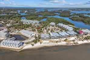 An aerial view of a coastal resort with multiple buildings, a beach, and a mangrove-filled bay.