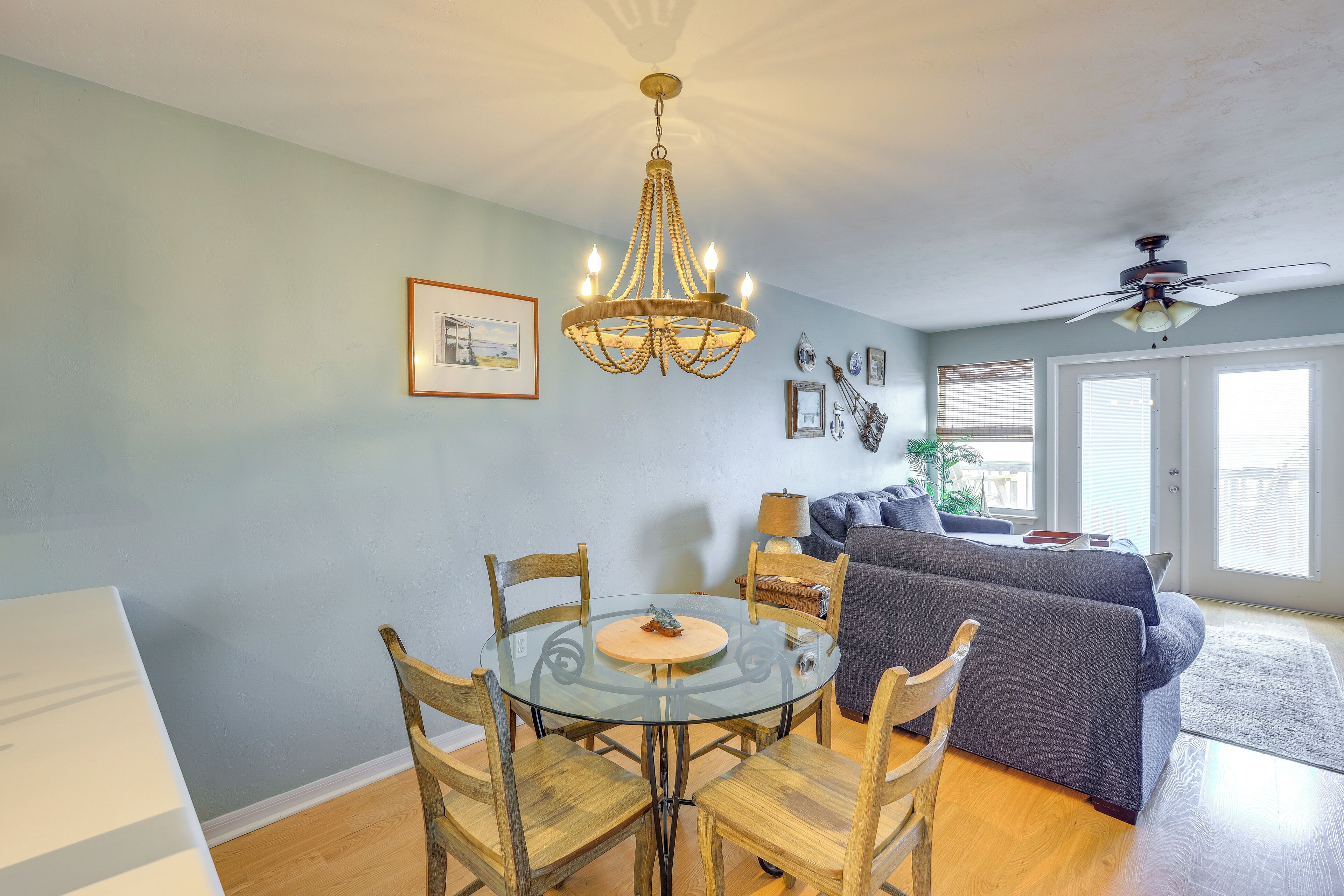 Un coin repas avec une table en verre, des chaises en bois, un lustre et un canapé en arrière-plan.