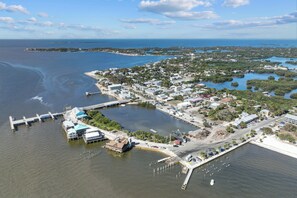 An aerial view of a coastal town with a marina, waterfront buildings, and a bridge connecting to the mainland.