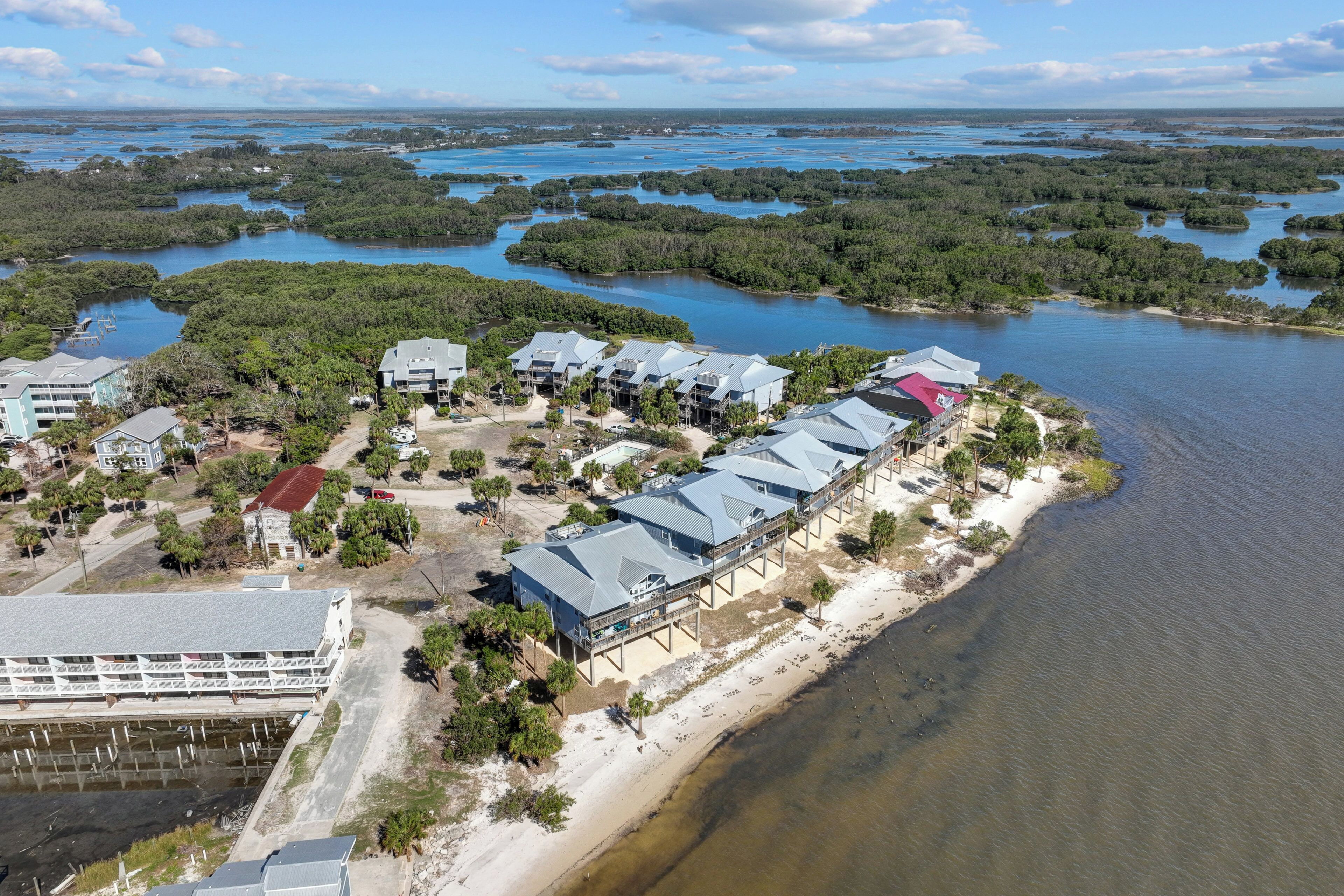 An aerial view of a coastal hotel with multiple buildings, a beach, and surrounding mangrove forests.
