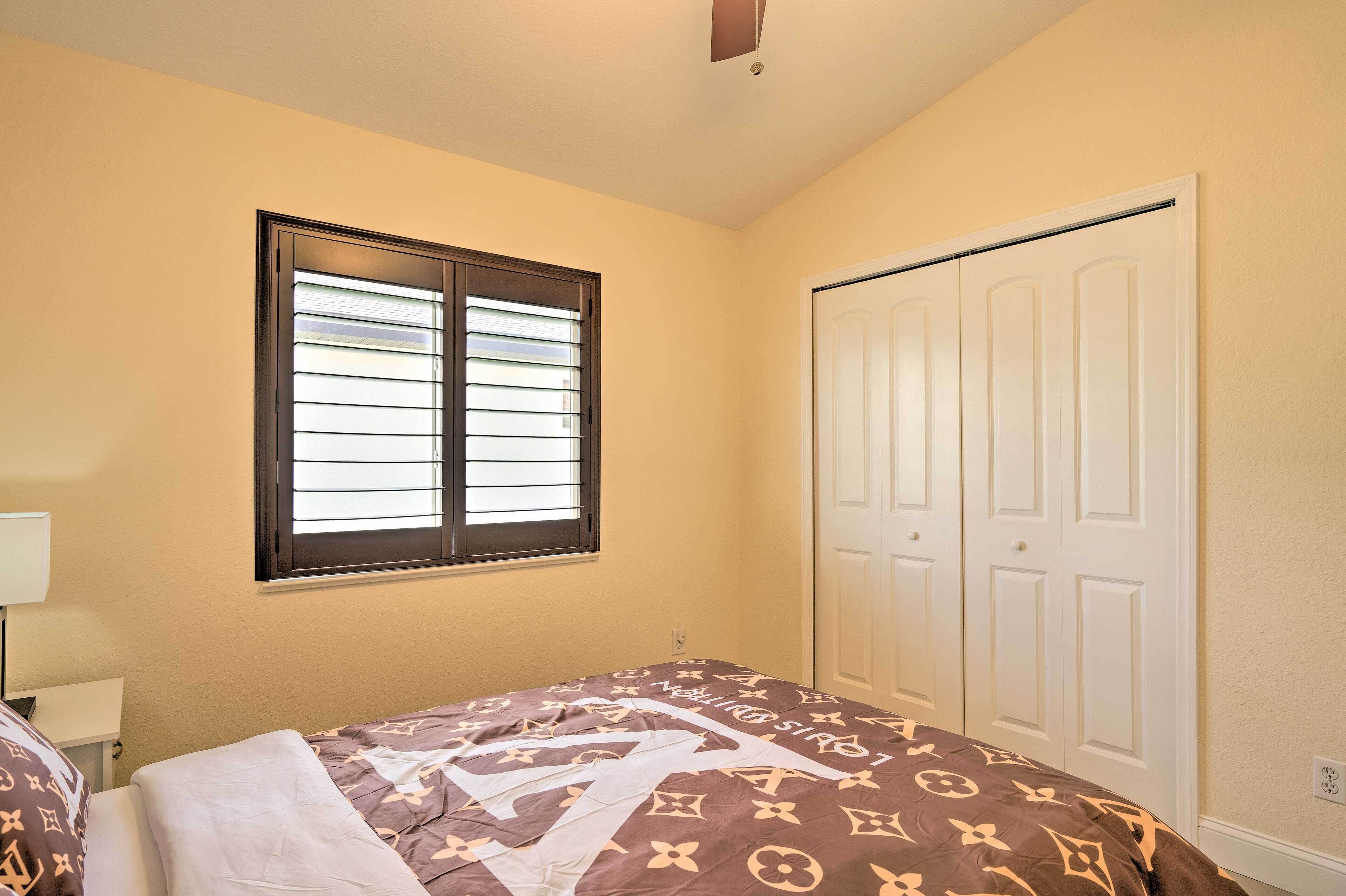 A bedroom with a bed, a window with blinds, a wardrobe, and a ceiling fan.