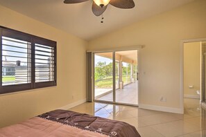 A bedroom with a bed, a large window with blinds, a ceiling fan, and a sliding glass door leading to a balcony. - Screened Patio: Canal-front Cape Coral Home (Cape Coral)