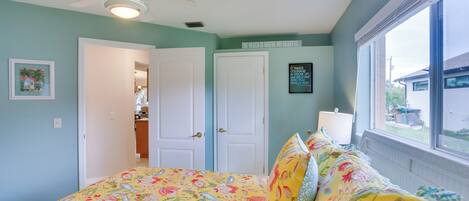 A bedroom with a floral bedspread, a ceiling fan, and a window with a view of the outside.