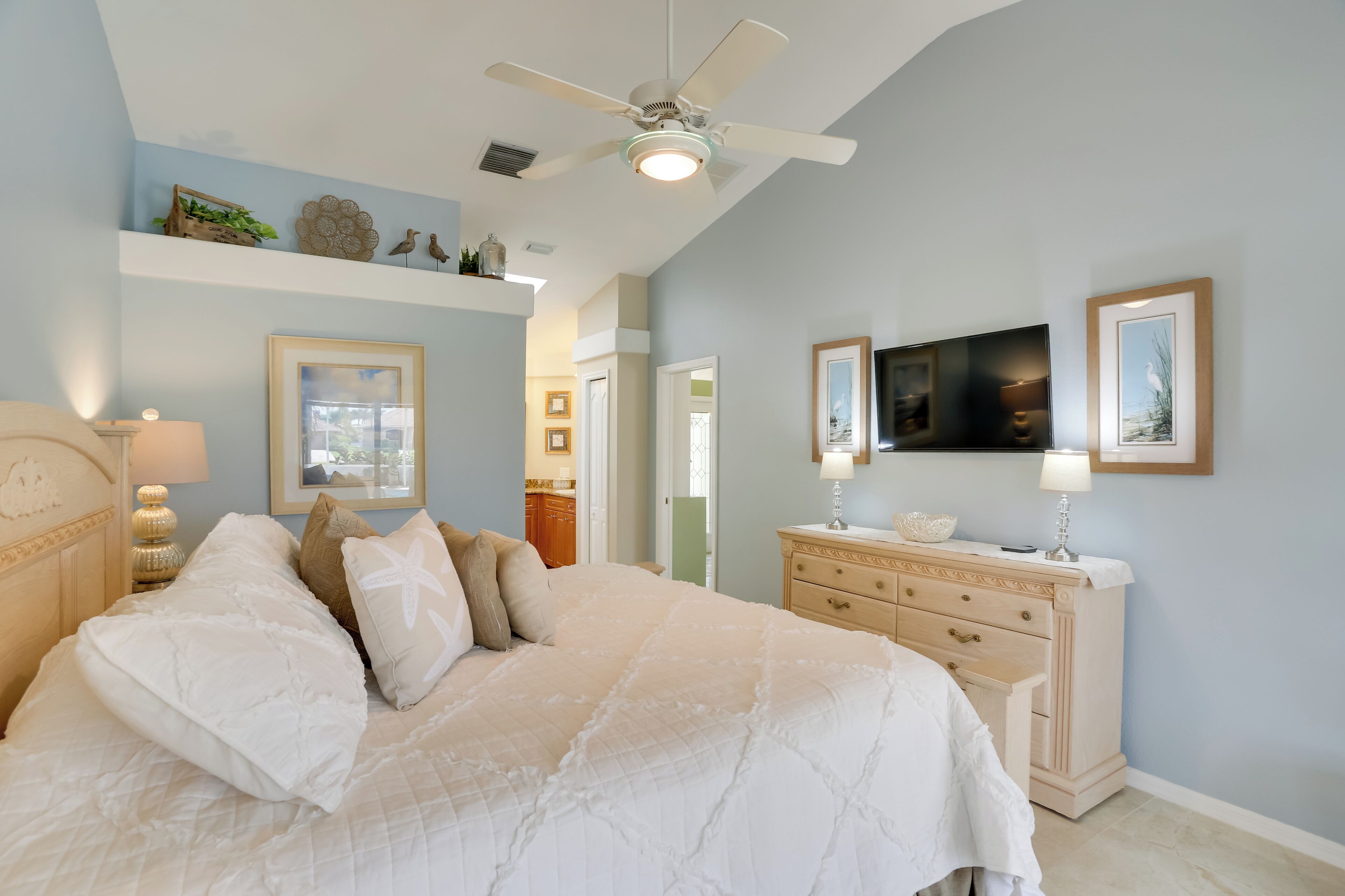A bedroom with a bed, dresser, ceiling fan, and artwork on the walls.