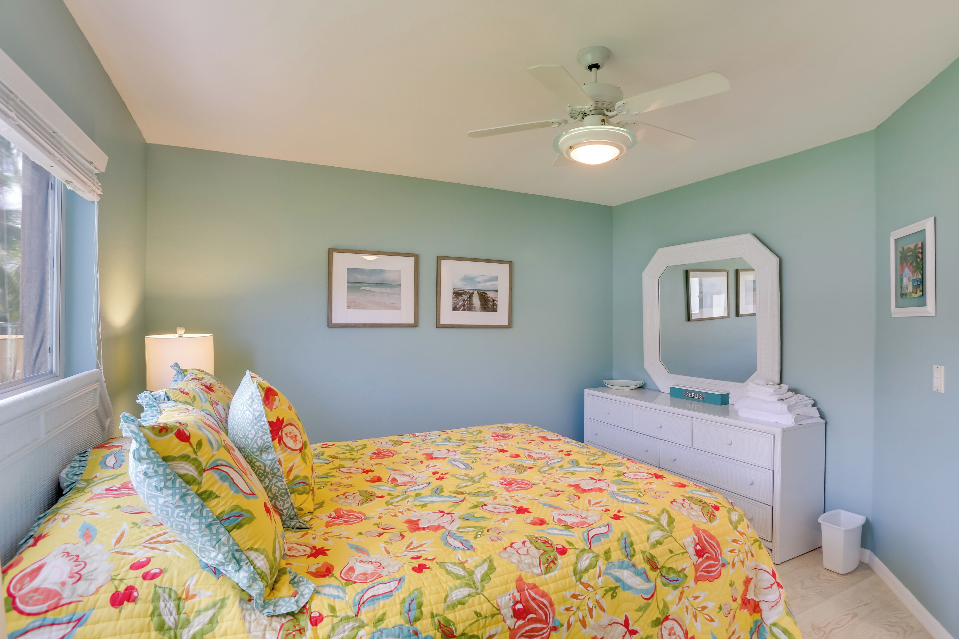 A bedroom with a bed, a ceiling fan, a dresser, and framed pictures on the wall.