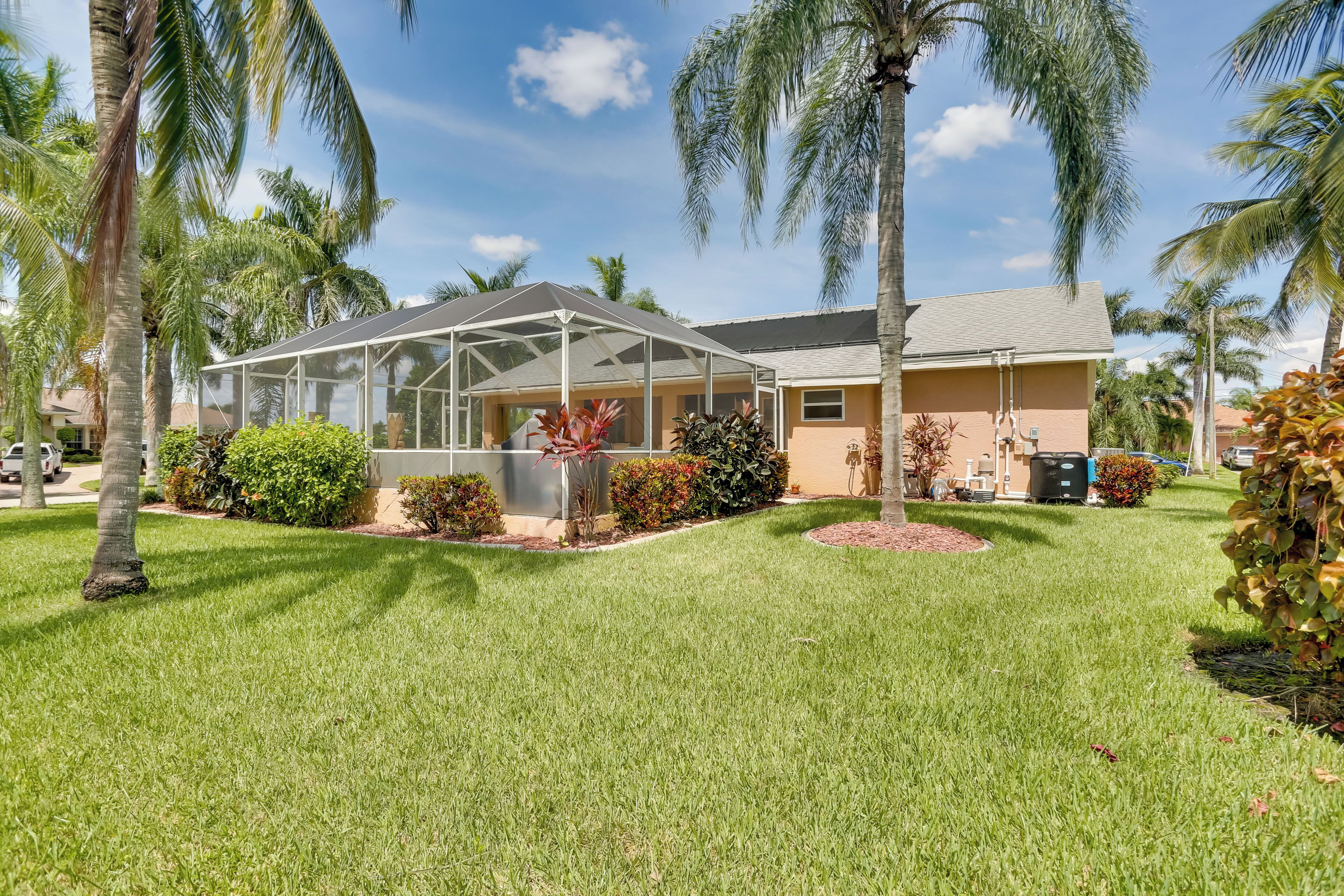 A house with a covered patio, surrounded by well-maintained grass and palm trees.