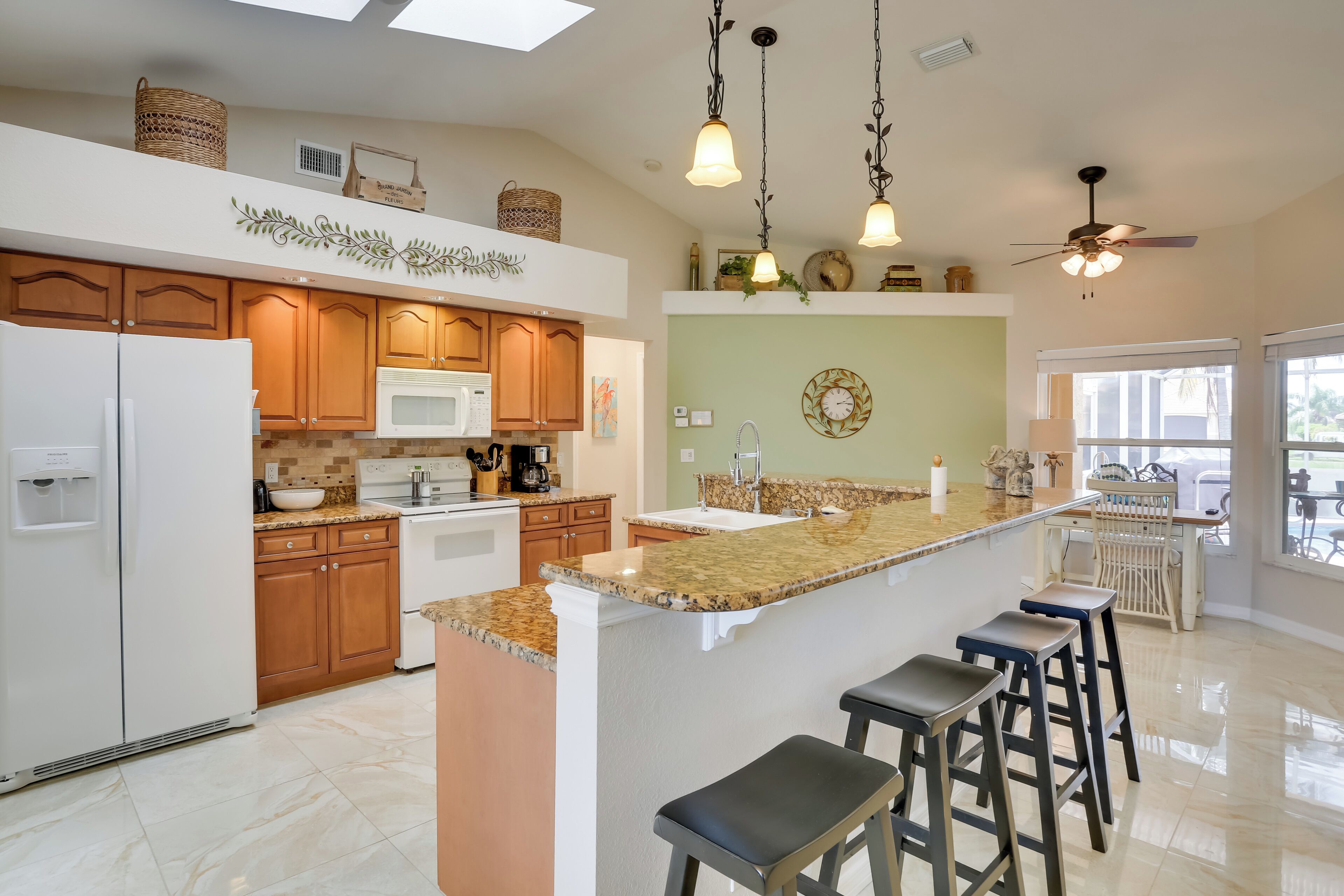 A spacious kitchen with wooden cabinets, a central island with stools, a ceiling fan, and pendant lighting.