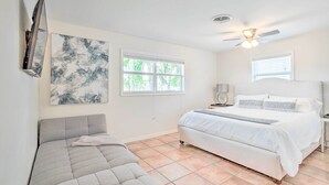 Une chambre à coucher avec un lit, un canapé, un ventilateur de plafond et des œuvres d’art accrochées au mur.