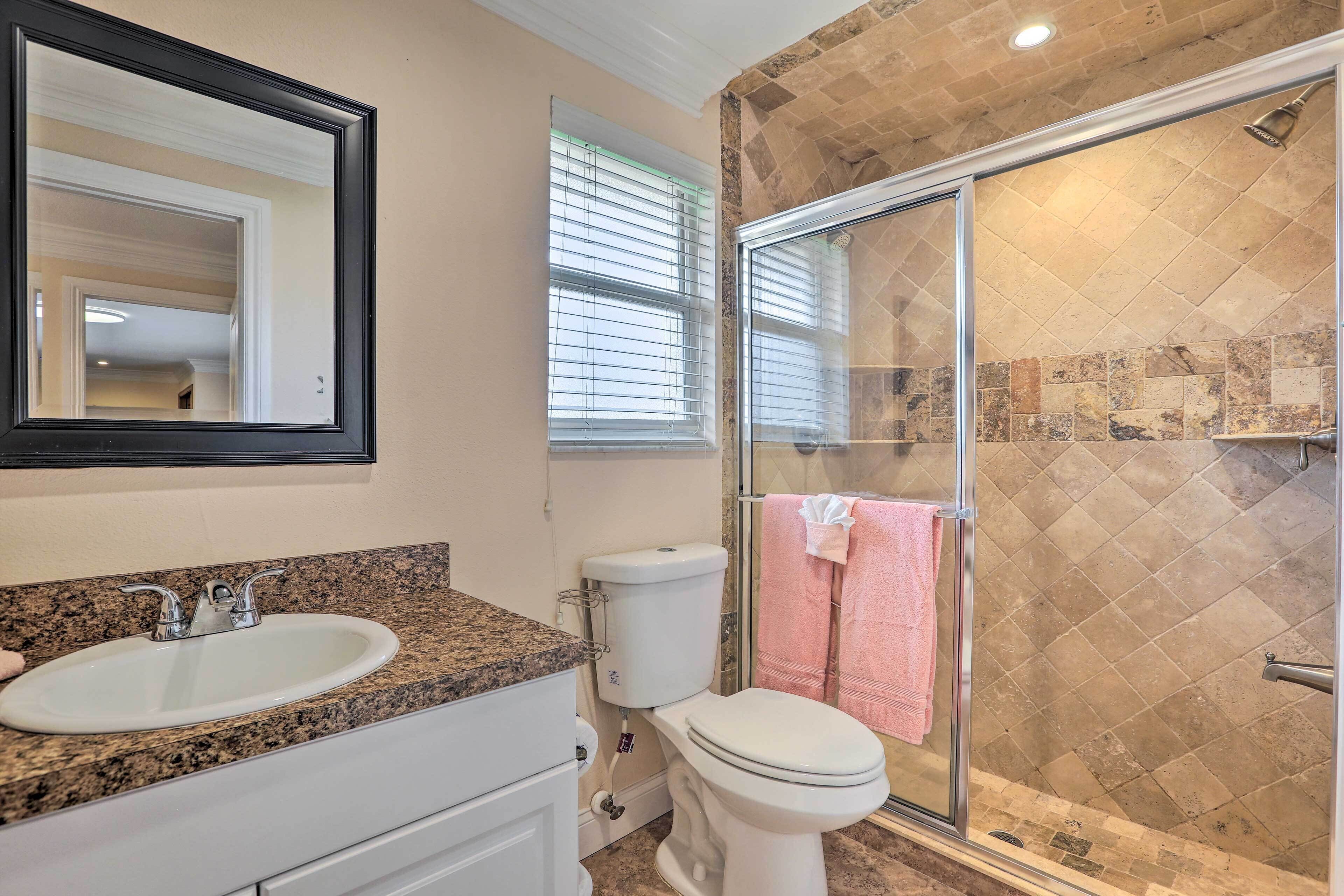 A bathroom with a granite countertop sink, a white toilet, and a glass shower enclosure with a tiled wall.