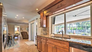 A kitchen with wooden cabinets, a stainless steel dishwasher, and a window with a view of the backyard. - Private Pool + Covered Patio: Cape Coral Haven! (Cape Coral)