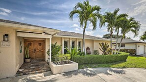 A residential house with a front entrance, a tiled porch, palm trees, and a well-maintained lawn. - Private Pool + Covered Patio: Cape Coral Haven! (Cape Coral)