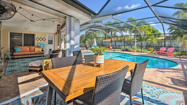 An outdoor patio with a wooden table and wicker chairs, a pool, and a covered seating area with a sofa and cushions. - Private Pool + Covered Patio: Cape Coral Haven! (Cape Coral)