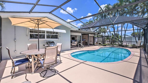 Un espace piscine doté d’un patio fermé par des baies vitrées, de mobilier d’extérieur et offrant une vue sur des palmiers.