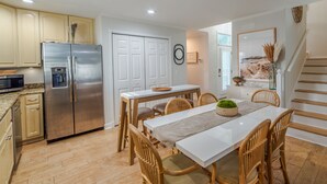 A modern kitchen with a stainless steel refrigerator, wooden cabinets, and a dining area with a white table and wicker chairs.