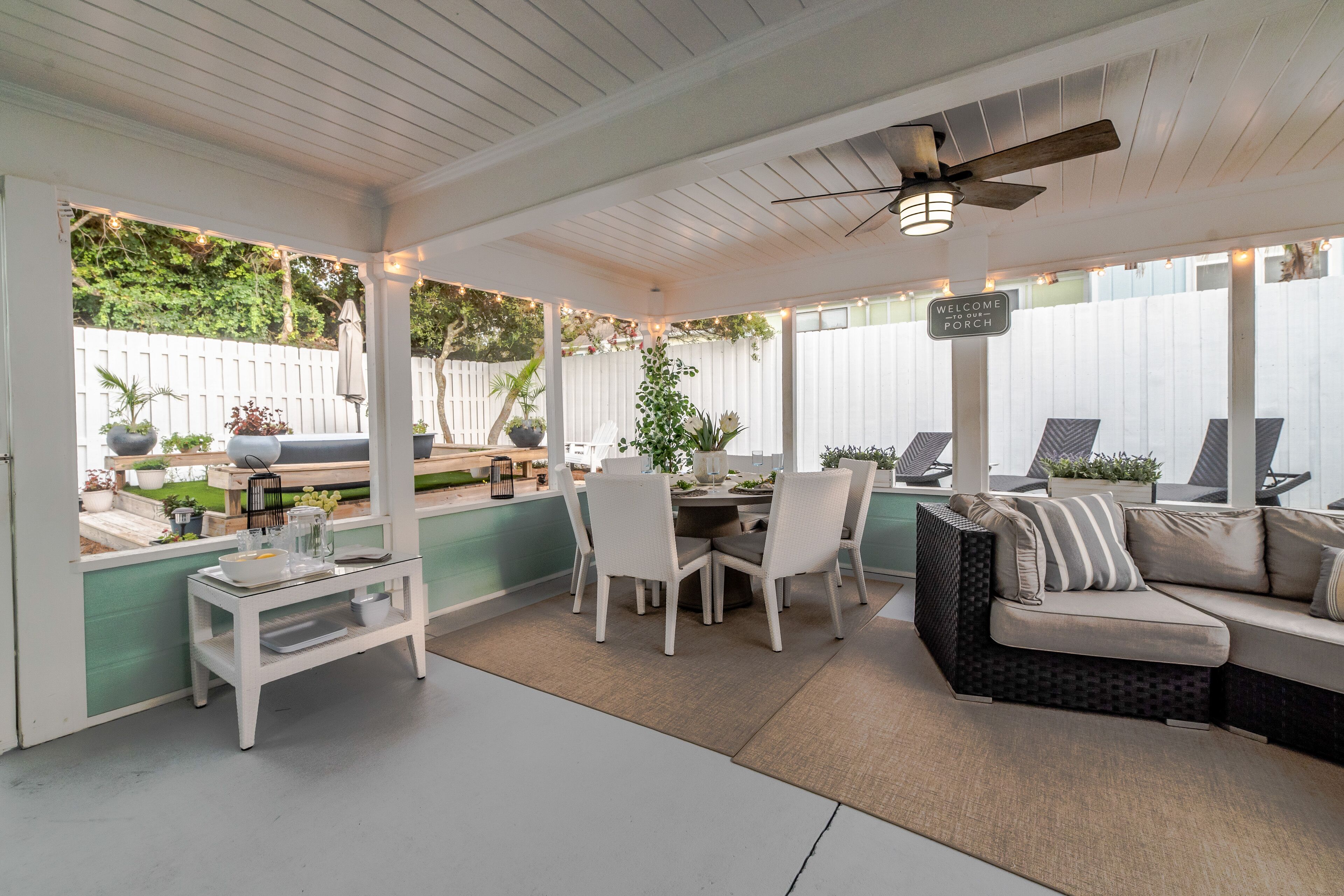 Ein überdachter Patio-Bereich mit Esstisch und Stühlen, einer Couch und einem Deckenventilator.