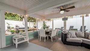 A covered patio area with a dining table and chairs, a sofa, and a ceiling fan.