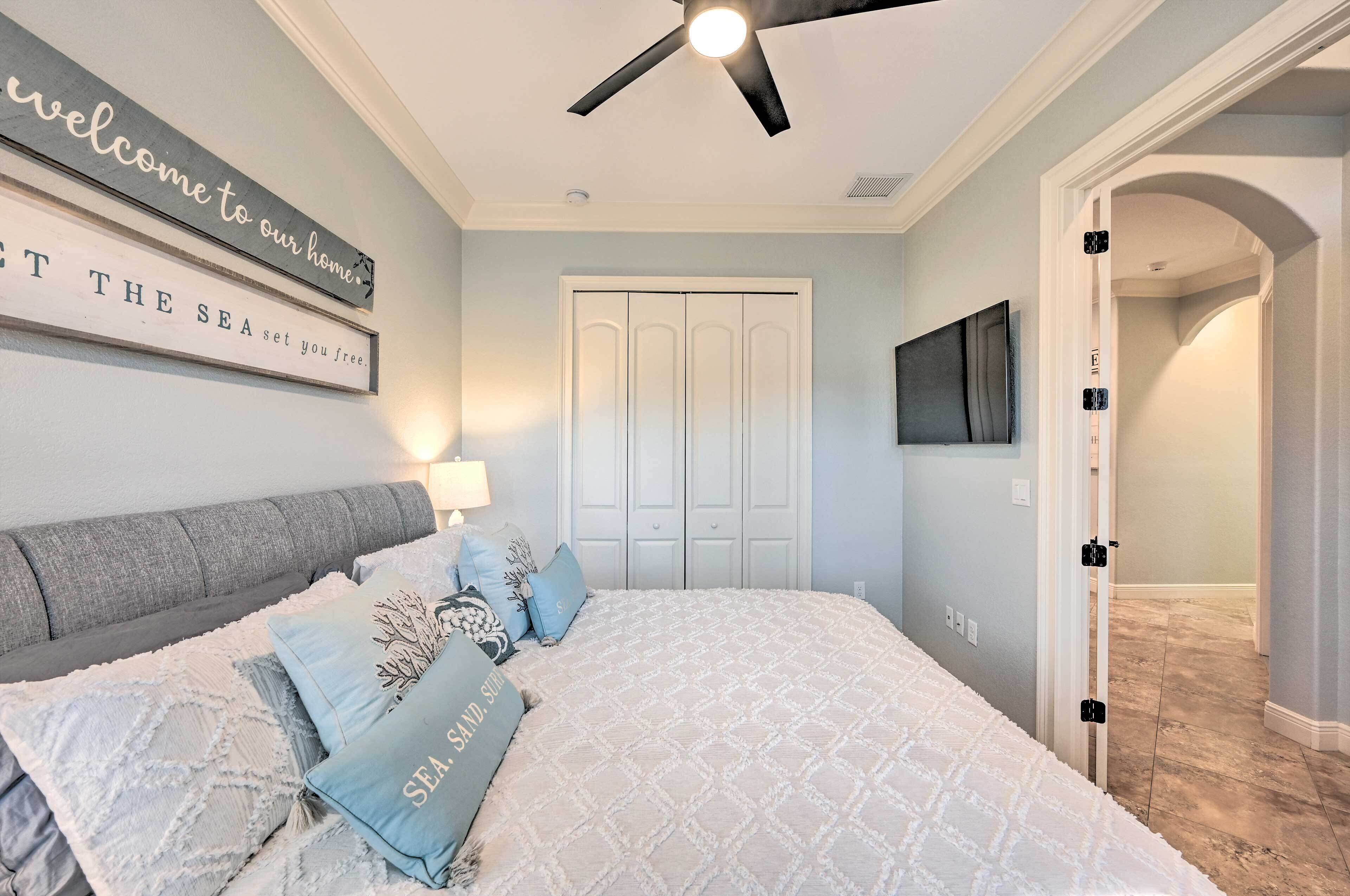 A bedroom with a bed, a ceiling fan, a wardrobe, and a wall-mounted TV.