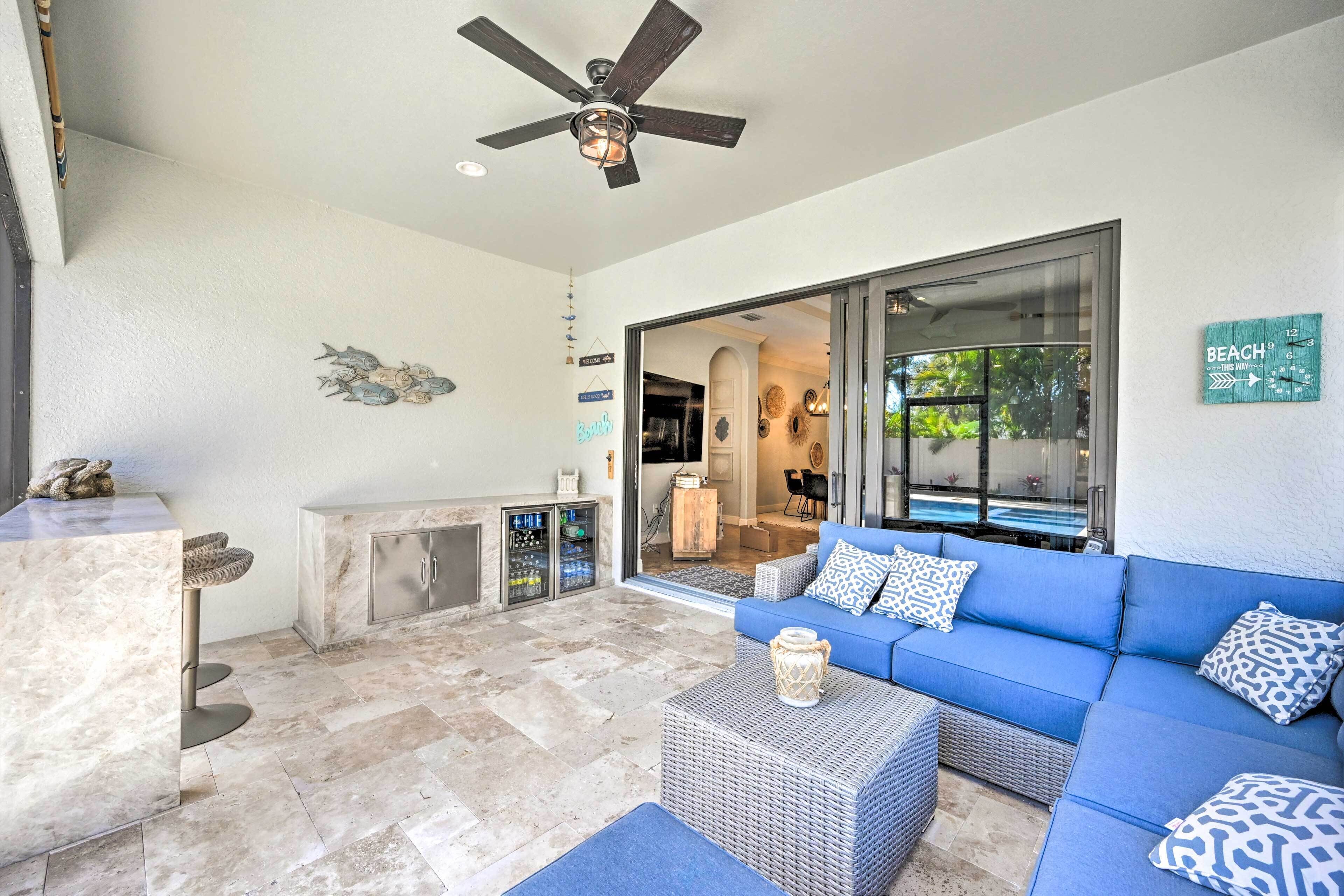 Un'ampia zona giorno con un divano blu, una ventola a soffitto e vista su una piscina tramite una porta in vetro.