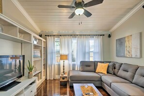 Un salon comprenant un canapé d’angle, un téléviseur, des étagères et un ventilateur de plafond.
