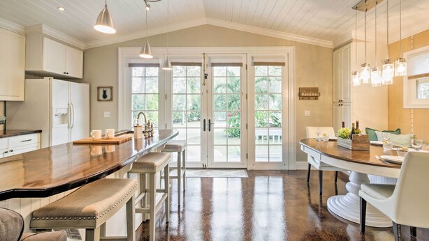 Cocina amplia con una isla grande, armarios blancos y vistas al exterior a través de puertas de vidrio.