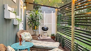 Un espacio al aire libre acogedor con mobiliario de mimbre, una mesa azul, una cerca de celosía blanca y una pérgola de madera con luces colgantes.