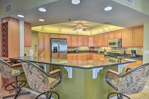 A kitchen with wooden cabinets, a stainless steel refrigerator, a microwave, and a large island with bar stools.