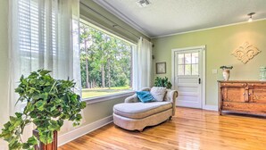 Um quarto com uma janela ampla, uma poltrona estofada, um armário de madeira e um vaso de plantas.